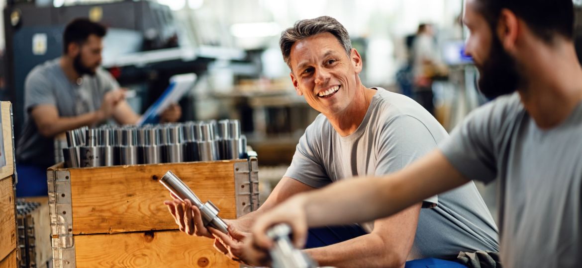 Happy manual workers talking while working together at steel factory.
