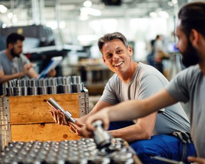 Happy manual workers talking while working together at steel factory.