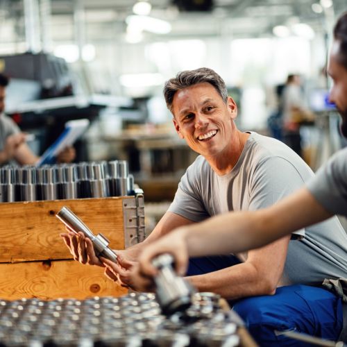 Happy manual workers talking while working together at steel factory.