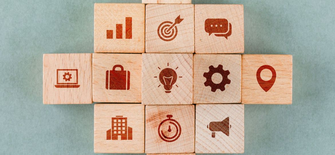 Business strategy concept with wooden blocks with icons on sage color background flat lay. horizontal image